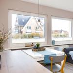 Wohn- und Essbereich mit Fenstern, Tisch, Stühlen und Sofa.
