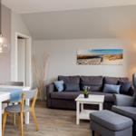 Wohn- und Essbereich mit Sofa, Stuhl und Tisch. Wandbilder zeigen Strandlandschaften.
