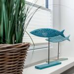 Zwei hölzerne Fische auf einem Fensterbrett neben einer Pflanze in einem Korb.