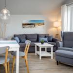 Wohn- und Essbereich mit grauem Sofa, Esstisch und Sessel. Holzboden und große Fenster.