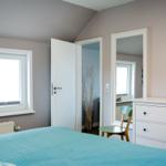 Schlafzimmer mit Bett, Schrank und Fenster. Tür führt in angrenzenden Raum.