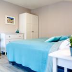 Schlafzimmer mit Bett, Schrank und Nachttisch. Wandbild und Pflanze sichtbar.