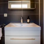 Badezimmer mit Waschbecken, Spiegel und Handtuchhalter an dunkler Wand