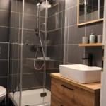 Dusche mit Glaswand, Waschtisch mit Holzschrank und Spiegel.
