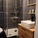 Badezimmer mit Dusche, Waschbecken und Holzschrank.