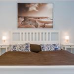Schlafzimmer mit weißem Bett, zwei Nachttischen und Wandbild