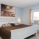 Schlafzimmer mit weißem Bett, Wandbild und Fenster mit Vorhängen.