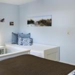 Schlafzimmer mit weißem Bett, blauen Wänden und Strandbildern an der Wand.