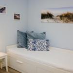 Ein Schlafzimmer mit weißem Bett, Kissen und Wandbildern an hellblauen Wänden.