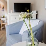 Ein blauer Sessel mit weißer Decke und Blumen in einem Glas auf einem Tisch.