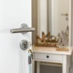 Schlüssel hängen an einer Tür mit Metallgriff. Im Hintergrund steht ein kleiner Schrank mit Dekoration.