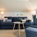 Living room with sofa, armchair, and table. Wall art and floor lamp visible.