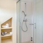 Shower with glass enclosure and built-in shelf for towels and toiletries.