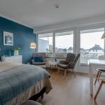 Schlafzimmer mit Bett, Sitzgelegenheiten und Tisch. Blick auf Balkon und Dachlandschaft.