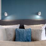 Doppelbett mit Kissen und blauer Wand mit Wandlampen.