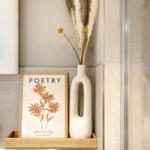 Badezimmer-Ecke mit Vase, Trockenblumen und Bild mit Blumenmotiv.