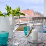 Terrasse mit Tisch, Gläsern, Kerze und Blumen. Hintergrund: Dachhäuser.