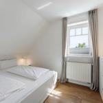 Schlafzimmer mit Dachschräge, weißem Bett, Fenster mit Vorhängen und Holzboden.