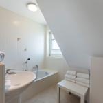 Badezimmer mit Badewanne, Waschbecken und Fenster unter Dachschrägen.