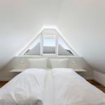 Zimmer mit Doppelbett unter Dachschräge und Dreifachfenster mit Blick auf Dächer.