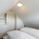 Zimmer mit Doppelbett, weißen Schränken und schrägen Wänden.