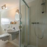 Badezimmer mit Dusche, Waschbecken und Toilette. Fenster und Heizkörper sichtbar.