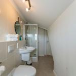 Badezimmer mit Dusche, Waschbecken und Toilette unter schrägem Dach
