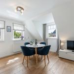 Dining room with round table, four chairs, TV, and windows.