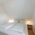 Schlafzimmer mit Doppelbett, weißen Laken und Holzboden. Dachschrägen an der Decke.