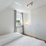 Schlafzimmer mit Dachschrägen, weißem Bett, Kleiderschrank und Fenster mit Blick auf Bäume.