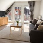 Wohnzimmer mit Sofa, Couchtisch und TV. Balkon mit Sitzgelegenheiten.