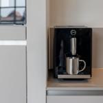 Eine schwarze Kaffeemaschine mit Edelstahlbecher auf einer Arbeitsfläche.