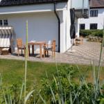 Terrasse mit Holztisch, Stühlen und Strandkorb. Hinterhof mit Steinmauer und Gras.