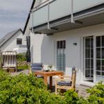 Terrasse mit Tisch, Stühlen und Liegestuhl. Hinterhof mit Pflanzen und Blick auf Haus.