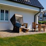 Terrasse mit Strandkorb, Tisch und Stühlen vor weißem Haus mit Steinmauer.