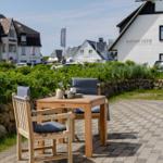 Terrasse mit Holztisch und Stühlen, Blick auf weiße Gebäude und Grünflächen.