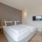 Schlafzimmer mit Doppelbett, Wand-TV und Holzboden.