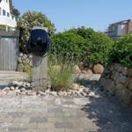 Eingangsbereich mit Pflanzen, Steinmauer und Grillplatz.