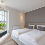 Doppelbett mit weißer Bettwäsche, Tür zum Balkon mit Gartenblick.
