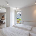 Schlafzimmer mit zwei Betten und Blick auf Balkon. Durchgang zur Küche sichtbar.