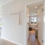 Hausflur mit Holzboden und Blick in Wohnzimmer mit Fenster und Sofa.