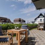 Terrasse mit Tisch und Stühlen, Blick auf Häuser und Strandkorb.