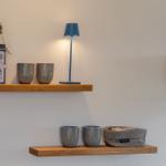 Zwei Holzregale mit Tassen, einer Lampe und einem Kaffeetöpfchen.