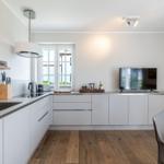 Moderne Küche mit weißen Schränken, Holzboden und Fenster mit Blick.