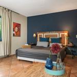 Schlafzimmer mit Bett, Wandbild und Fenster mit Blick auf Garten.