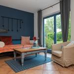 Ein Raum mit Bett, Couch und Tisch. Durch Fenster blickt man auf Garten.