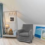 Zimmer mit grauem Sessel, Kleiderständer und Fenster mit Blick auf Grün.