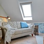 Ein Sofa mit Kissen und Decke unter einem Dachfenster. Ein Koffer und ein Bild sind sichtbar.