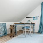 Schlafzimmer mit Schreibtisch, Stuhl und Koffer. Fenster mit Vorhang und Wandbild.