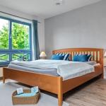 Schlafzimmer mit Holzbett, blauen Kissen und großem Fenster mit Blick auf Bäume.